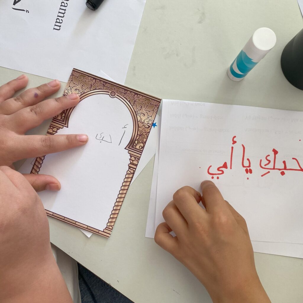 Deux enfants écrivent une carte pour la fête des mères en calligraphie arabe.
